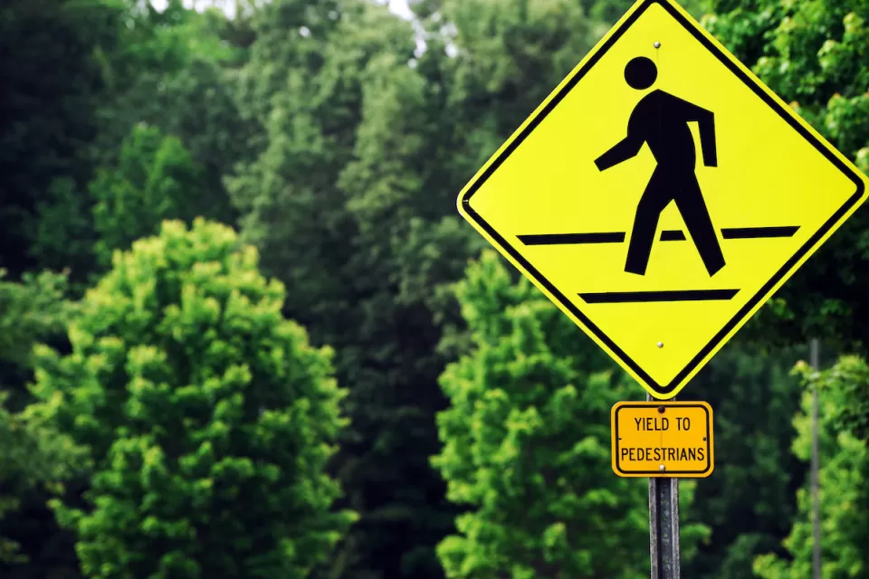 Yellow 'Yield to pedestrians' sign with graphic sign of person walking across street.